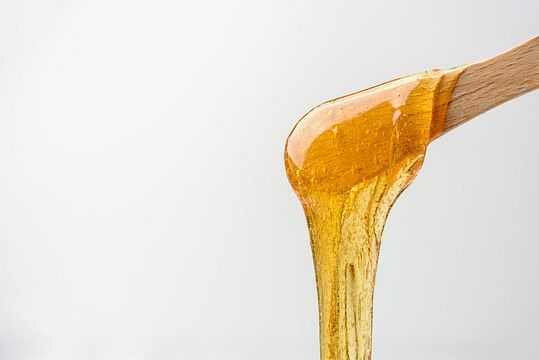 Wooden spatula drizzling smooth, golden honey.