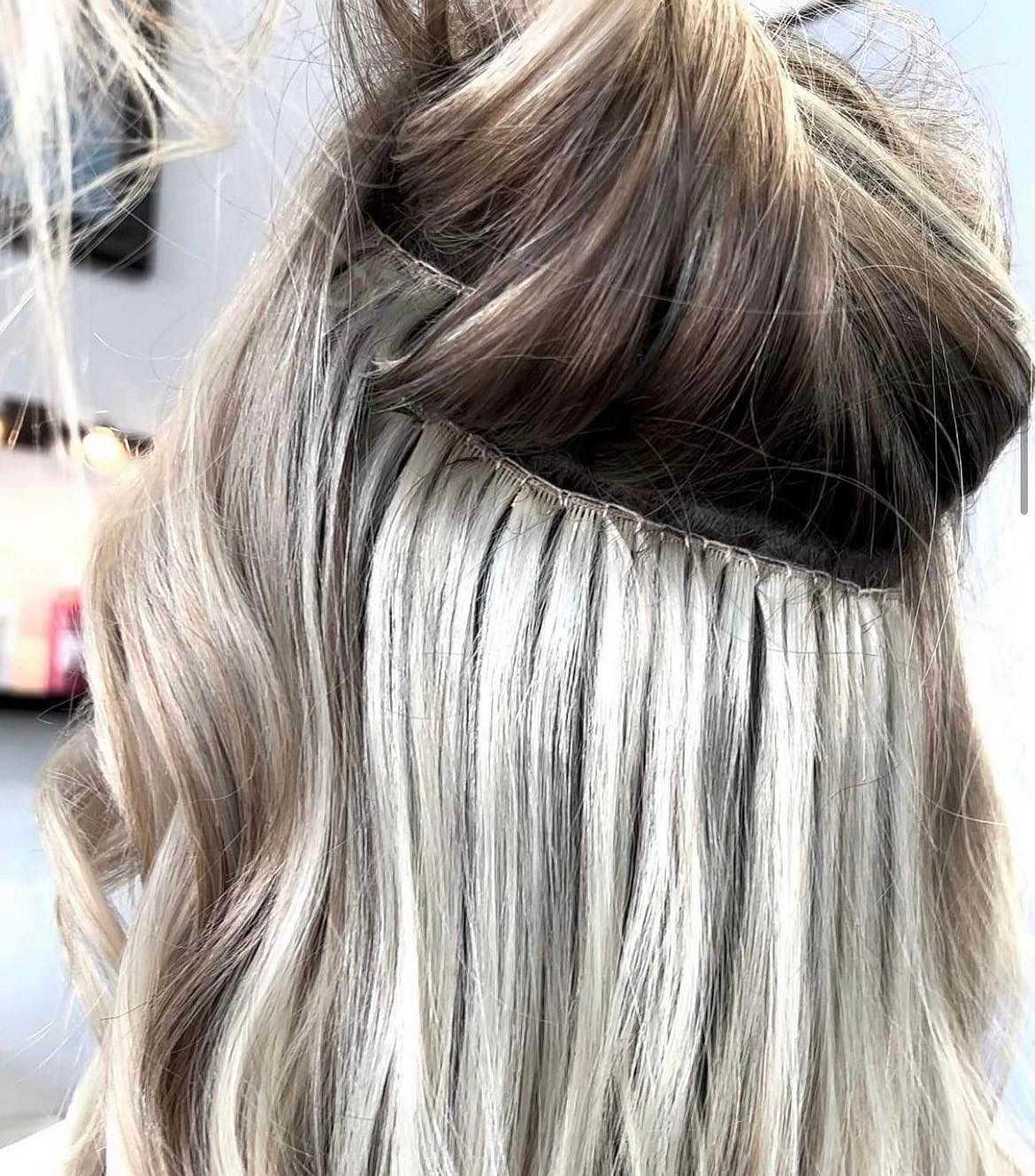 Hair extensions being applied to blonde hair in a salon setting.