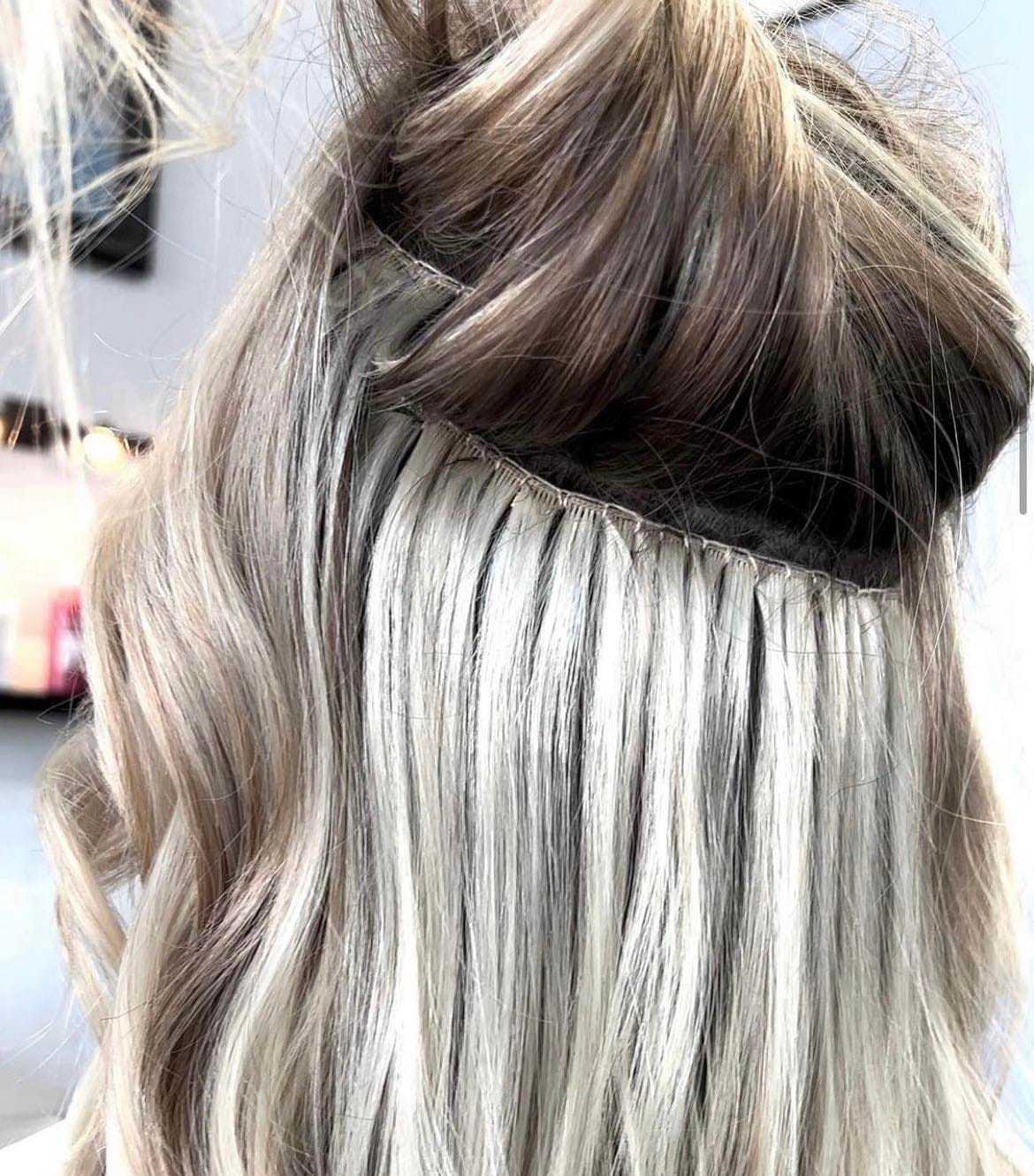 Hair extensions being applied to blonde hair in a salon setting.